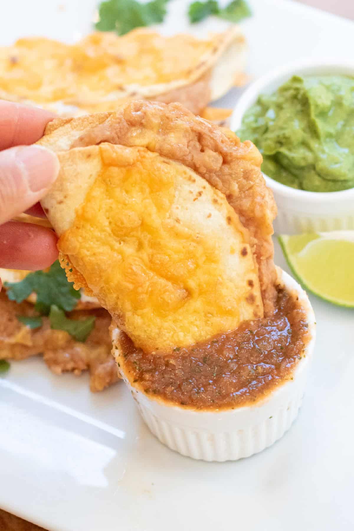 a hand holding a crispy taco being dunked into salsa.