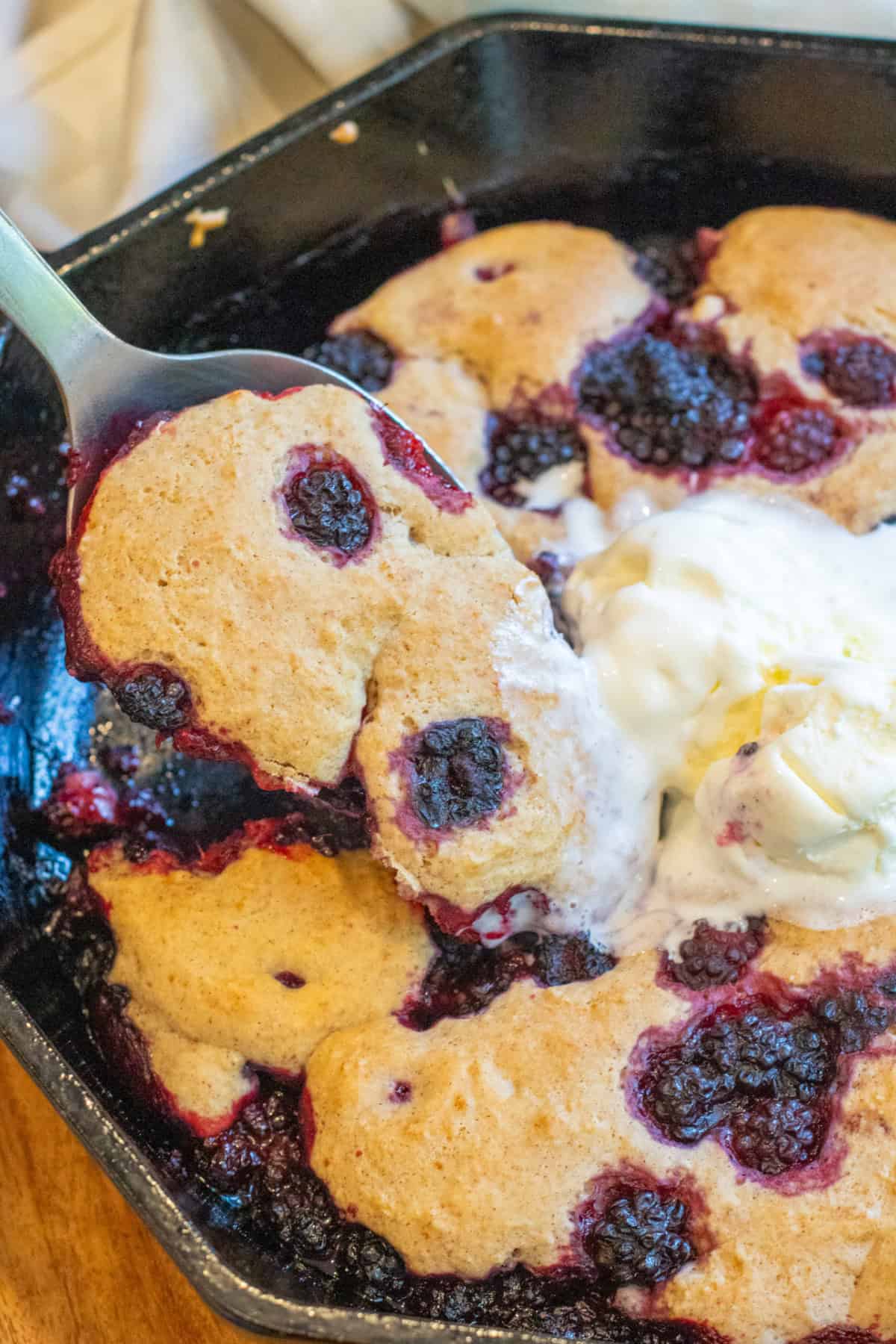 a spoon scooping out some blackberry cobbler from a skillet.