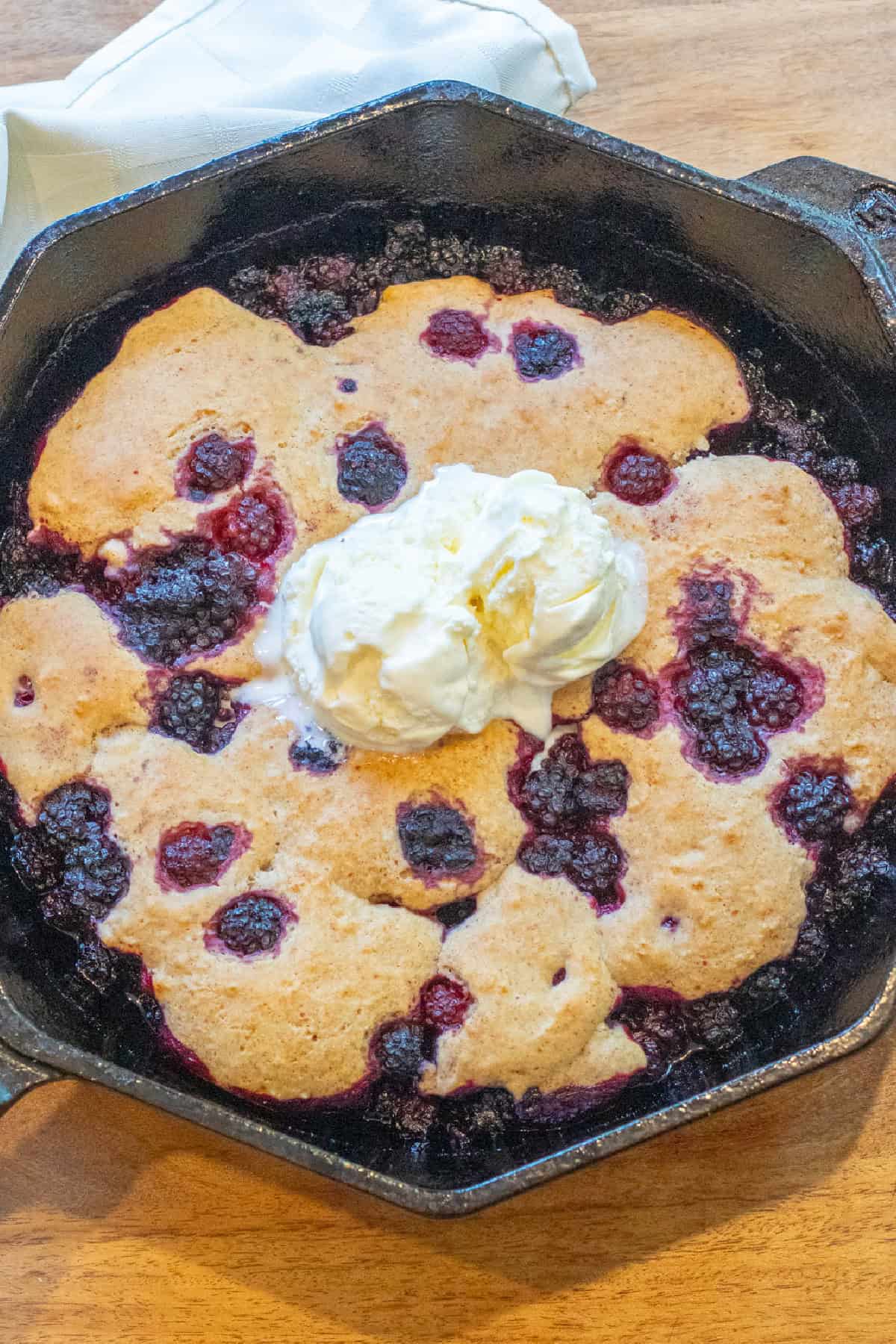 blackberry cobbler in a skillet with vanilla ice cream on top.
