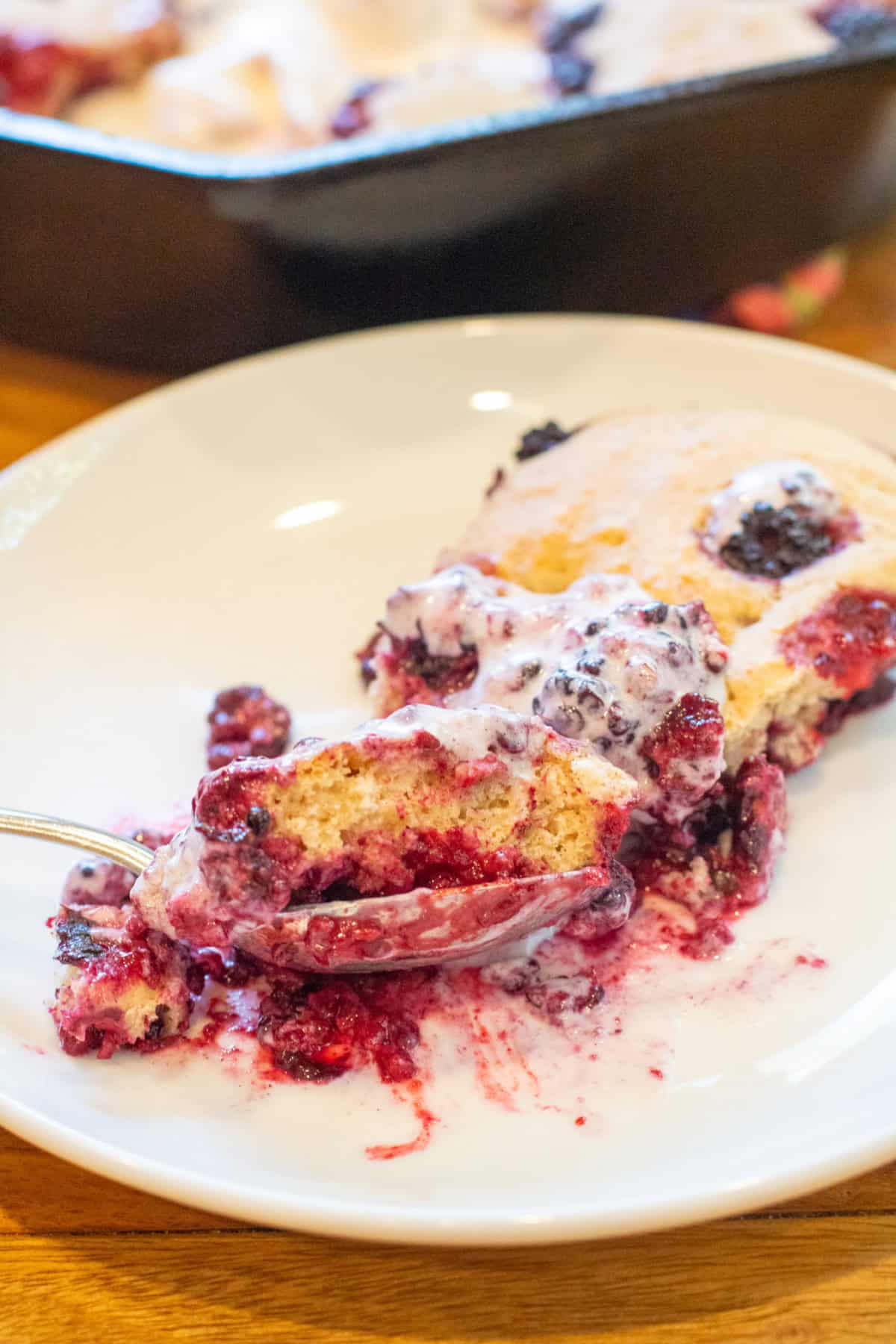 a plate of cobbler with a spoon in front of a cast iron with the  cobbler.