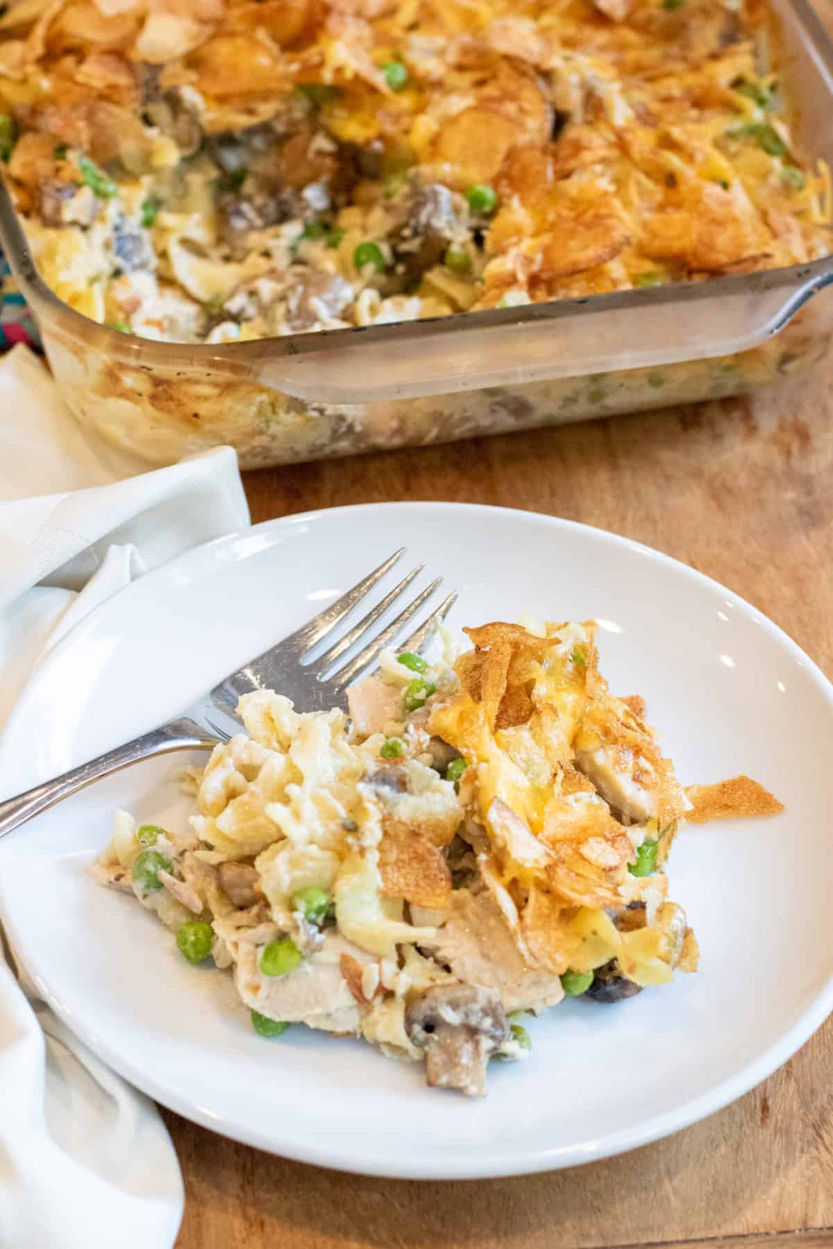 a plate of tuna noodle casserole with a fork in front of a casserole dish.
