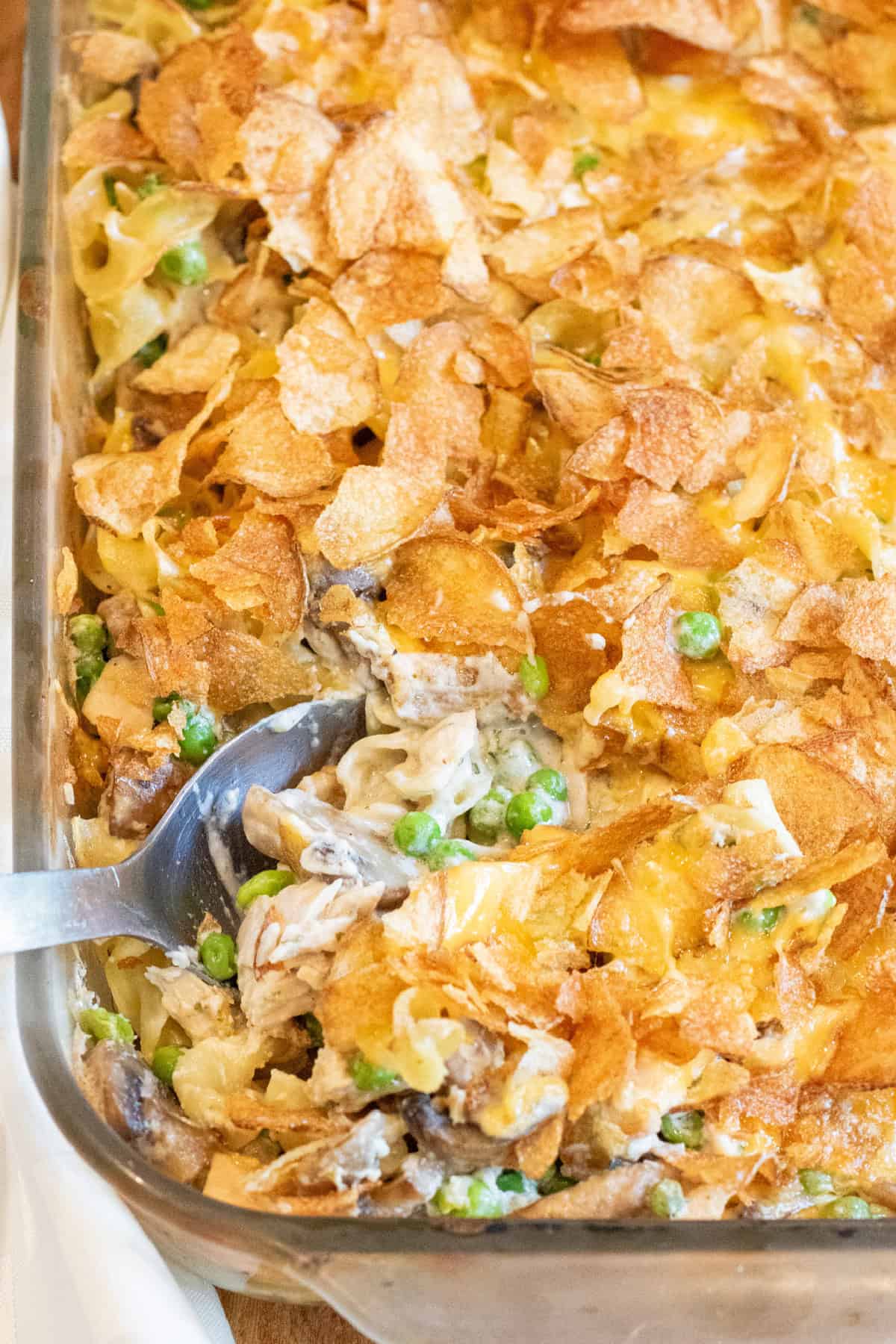 a spoon in a casserole with potato chips and peas, mushrooms, noodles, and tuna.