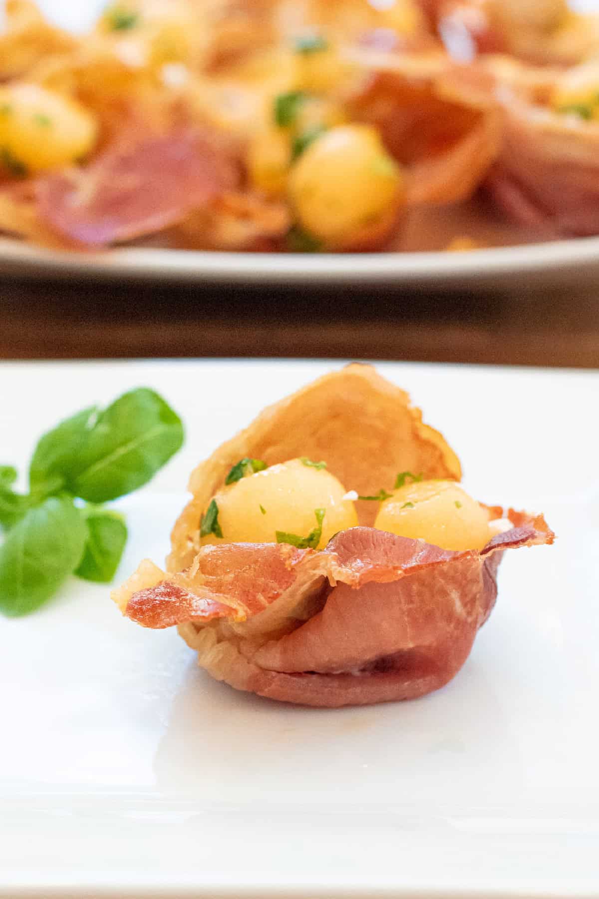 a plate with two baked prosciutto cups with melon and basil.