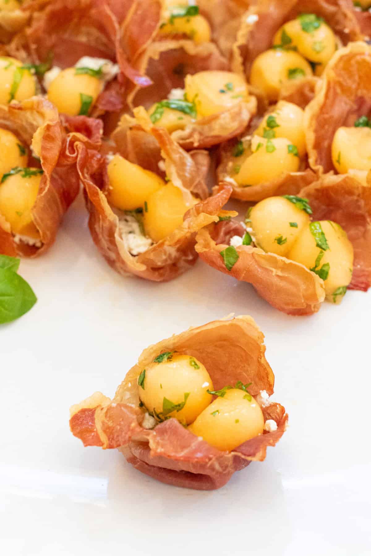 a plate with a baked prosciutto cups with melon and basil in front of others.