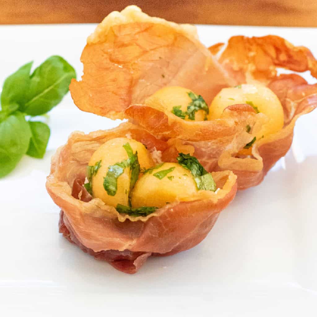 a plate with two baked prosciutto cups with melon and basil.
