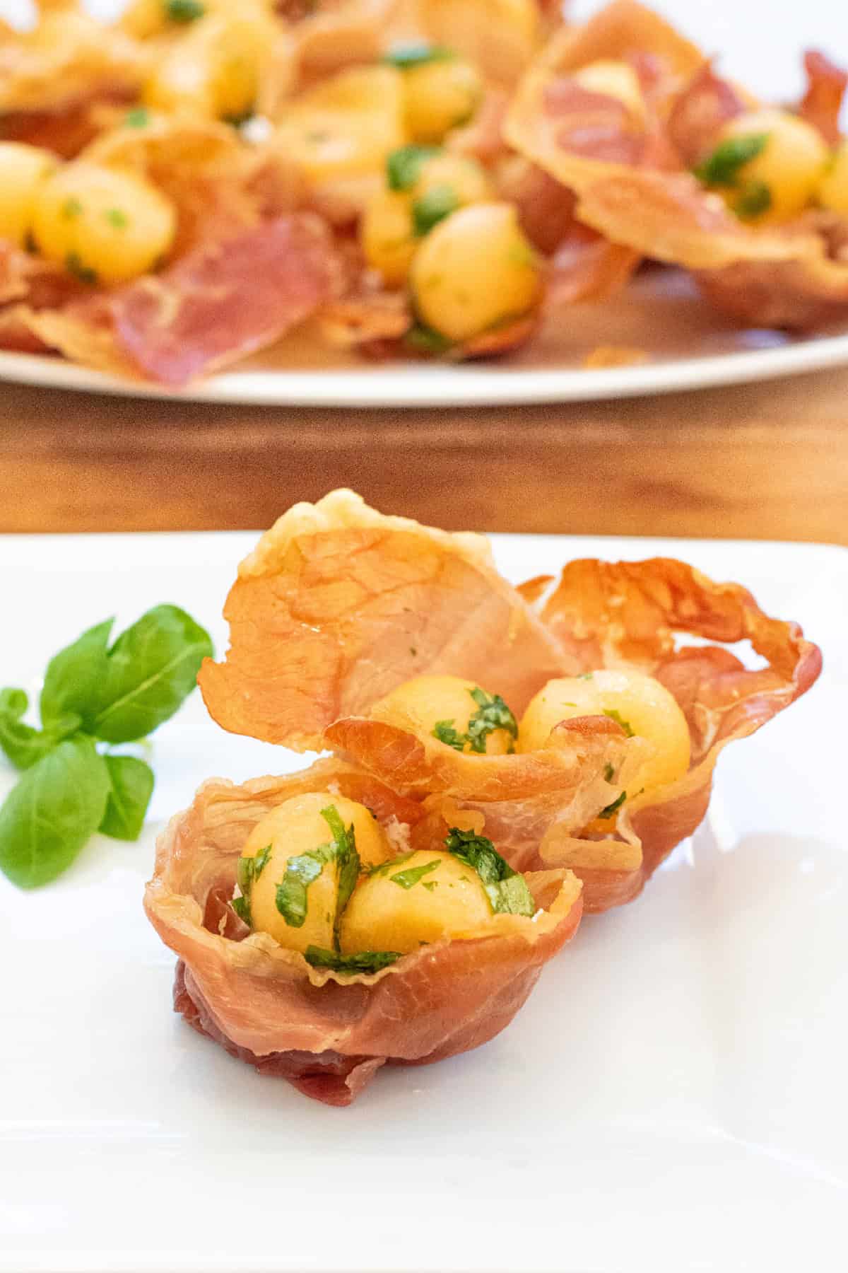 a plate with two baked prosciutto cups with melon and basil.