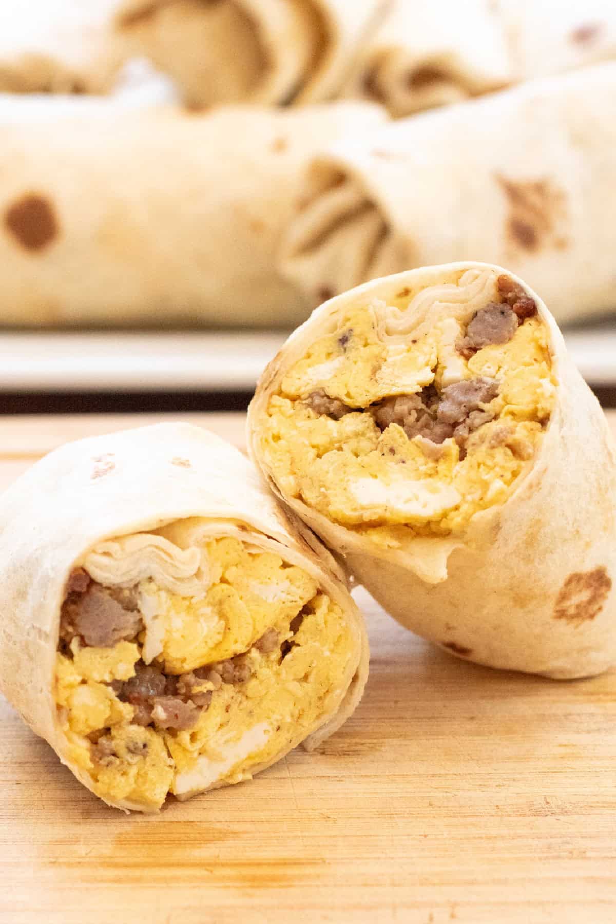 a halved egg and sausage breakfast burrito on a cutting board.