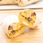 a halved egg and sausage breakfast burrito on a cutting board.
