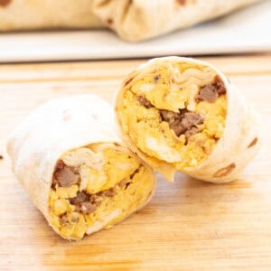 a halved egg and sausage breakfast burrito on a cutting board.