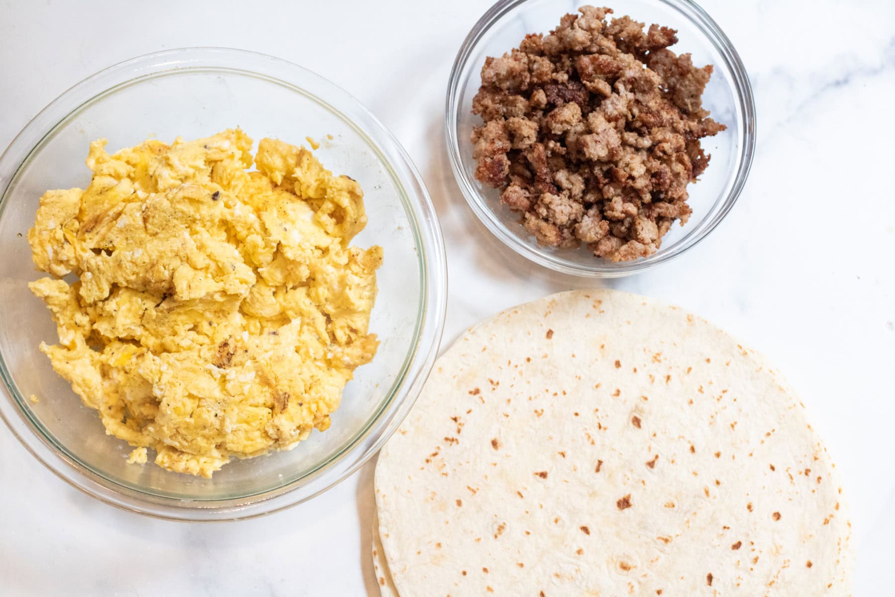 a bowl of scrambled eggs and cooked sausage and flour tortillas. 