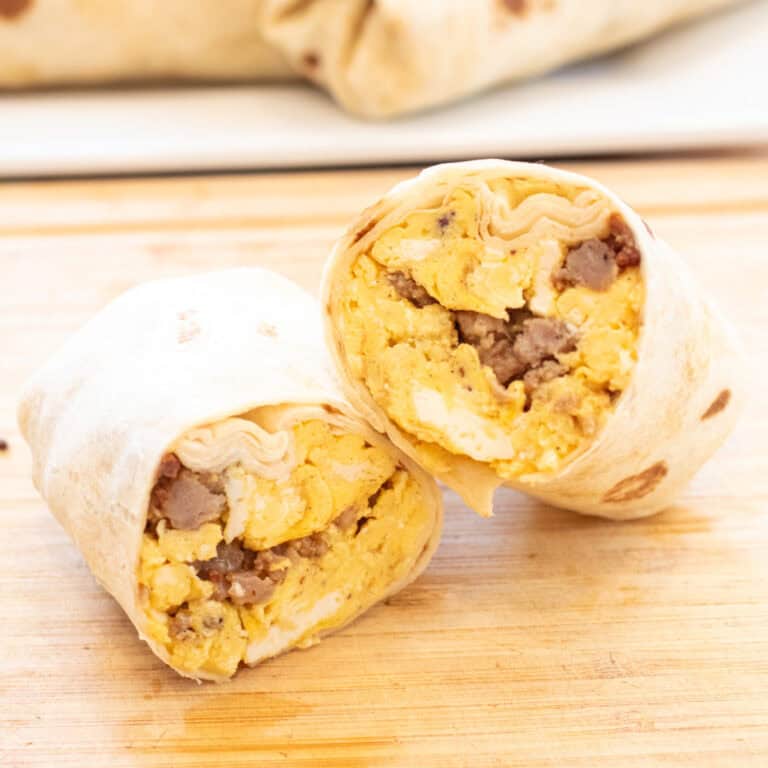 a halved egg and sausage breakfast burrito on a cutting board.