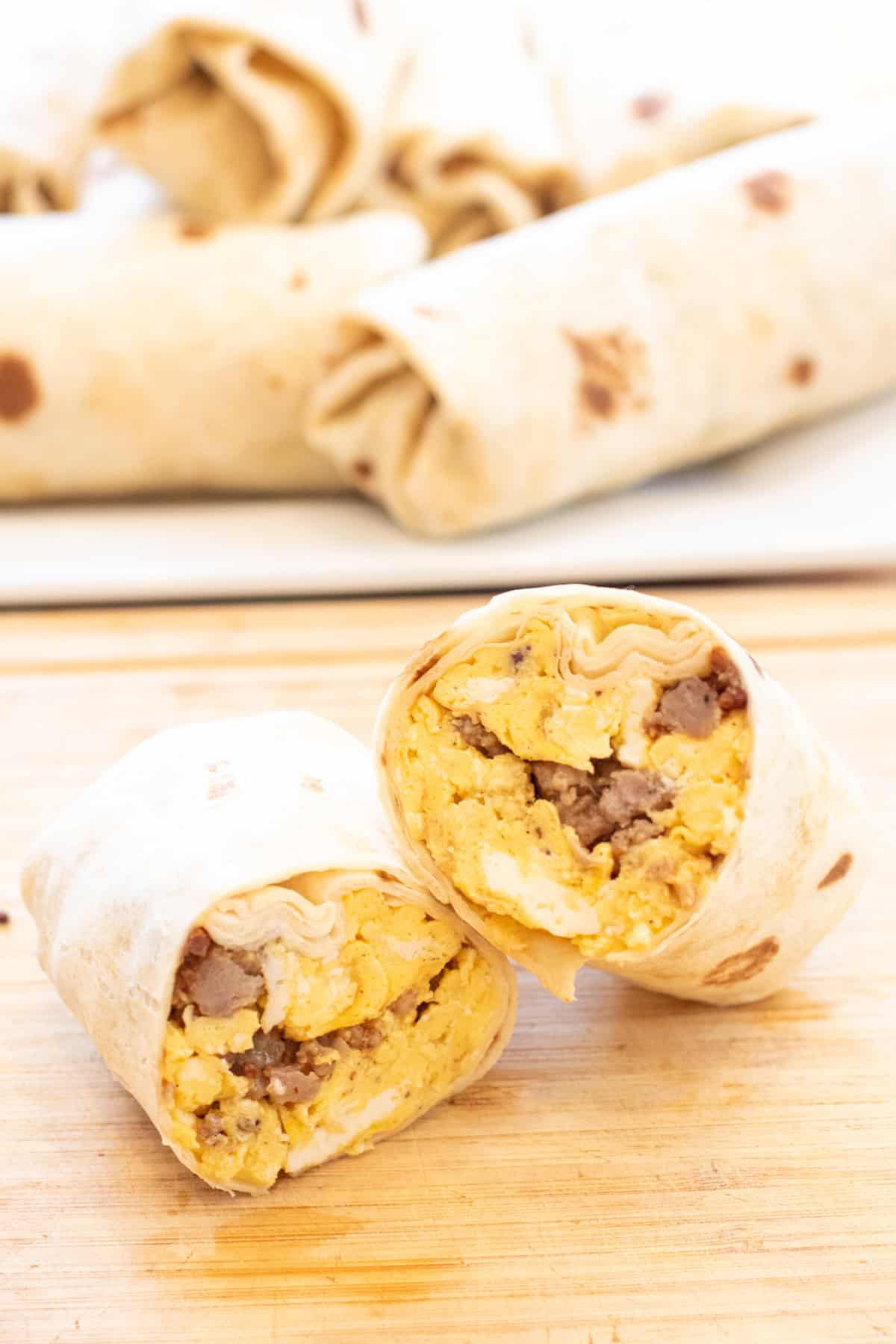 a halved egg and sausage breakfast burrito on a cutting board.
