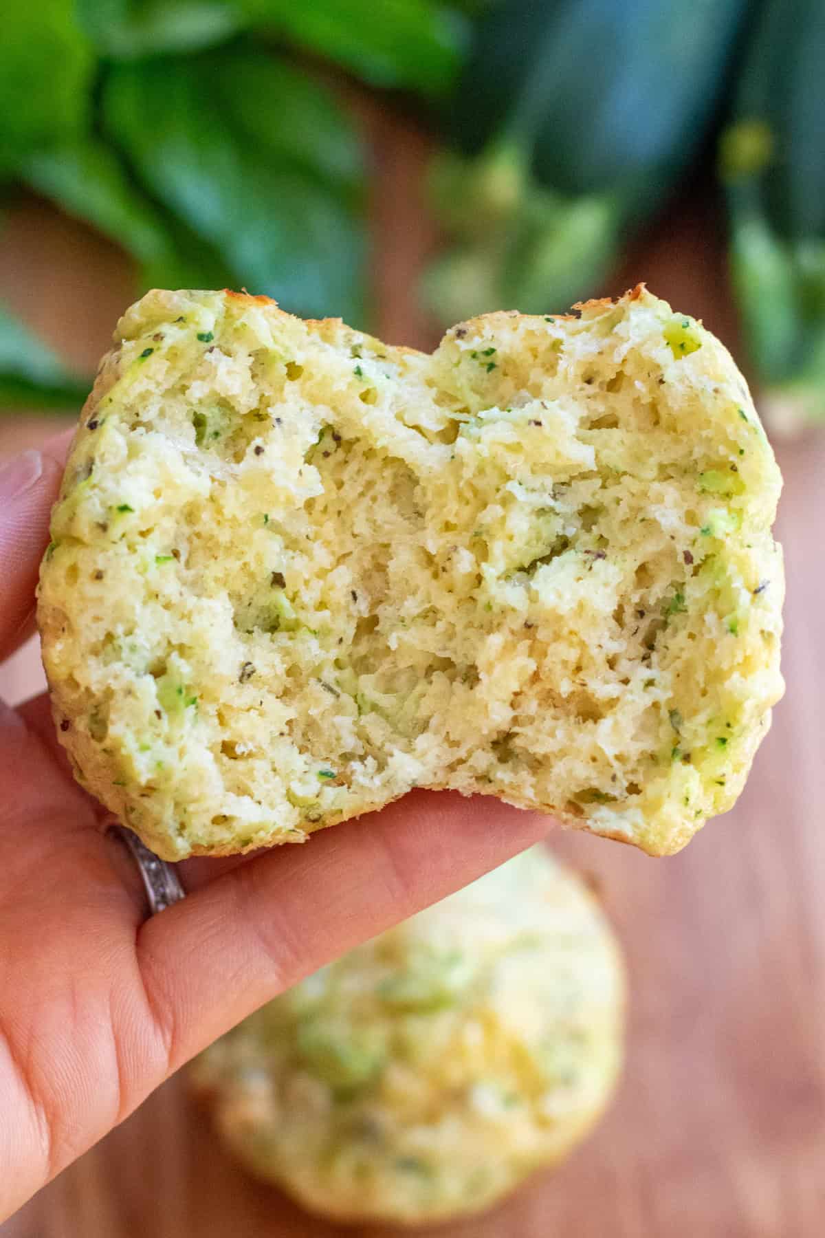 a hand holding a muffin with zucchini split in half.