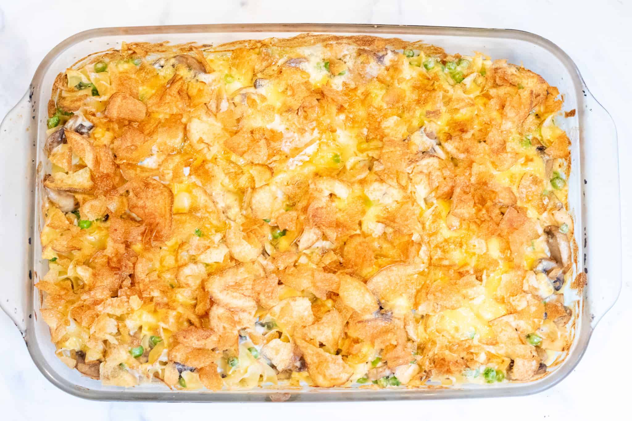 a baking dish with unbaked casserole with potato chips and tuna noodles and peas.