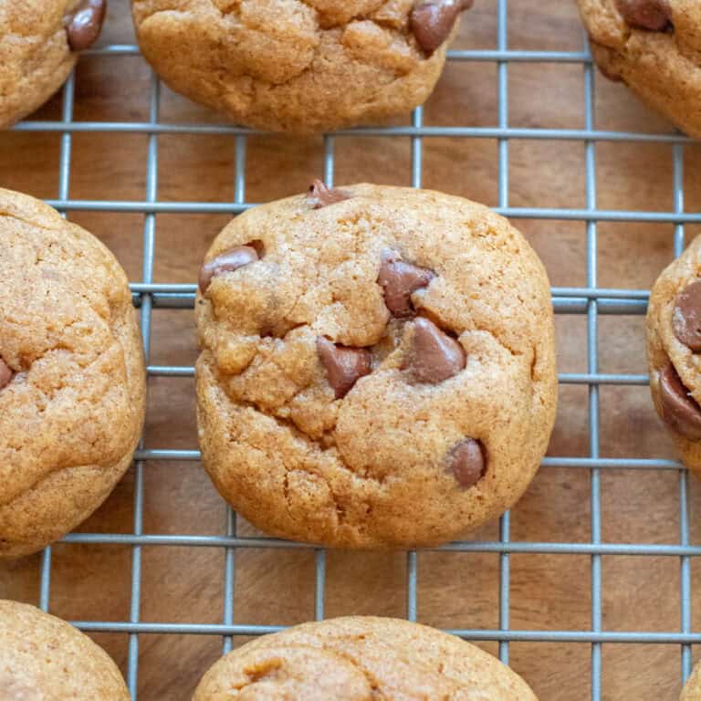 a round thick chocolate chip cookie on a cooling rack with other cookies.