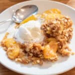 a plate of peach crisp with vanilla ice cream and a spoon.