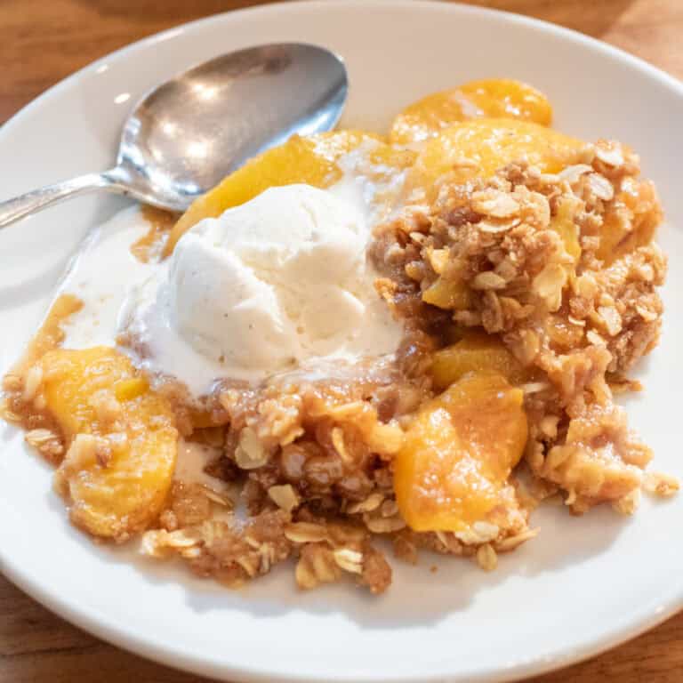 a plate of peach crisp with vanilla ice cream and a spoon.