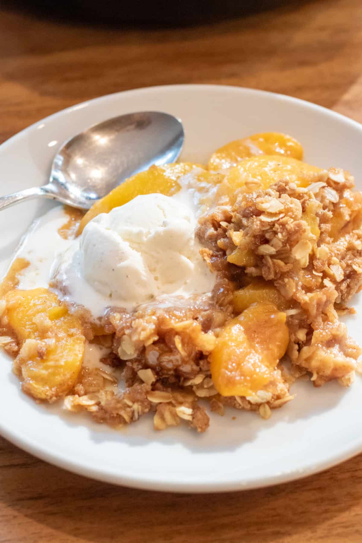 a plate of peach crisp with vanilla ice cream and a spoon.