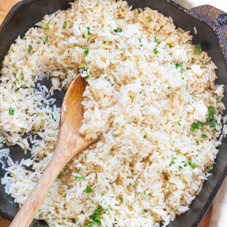a cast iron of cooked white rice with parsley and a wooden spoon.