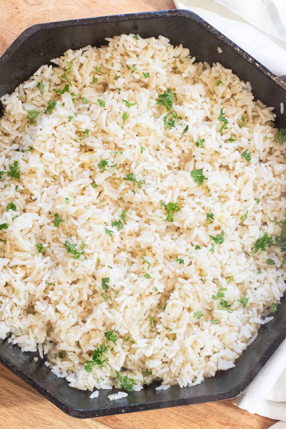 a cast iron skillet of cooked fluffed white rice with parsley.
