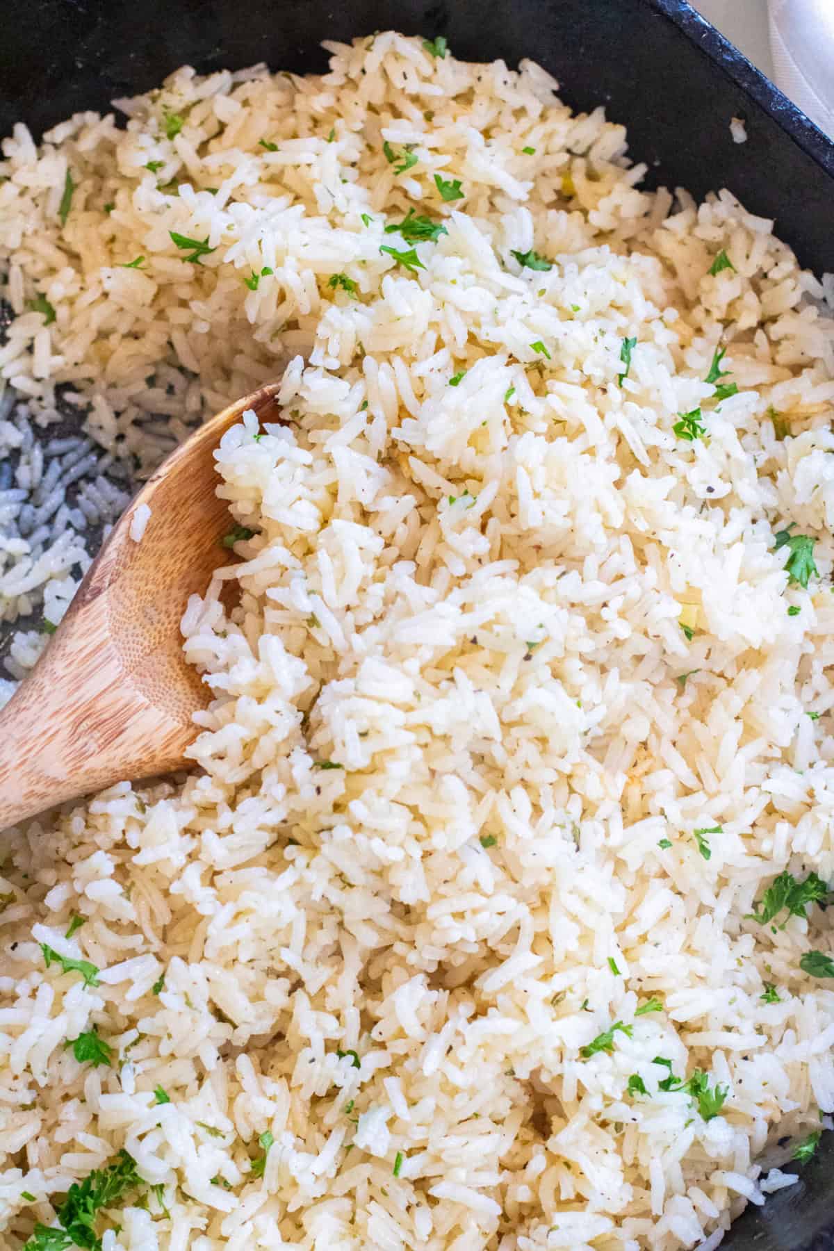 a cast iron of cooked white rice with parsley and a wooden spoon.
