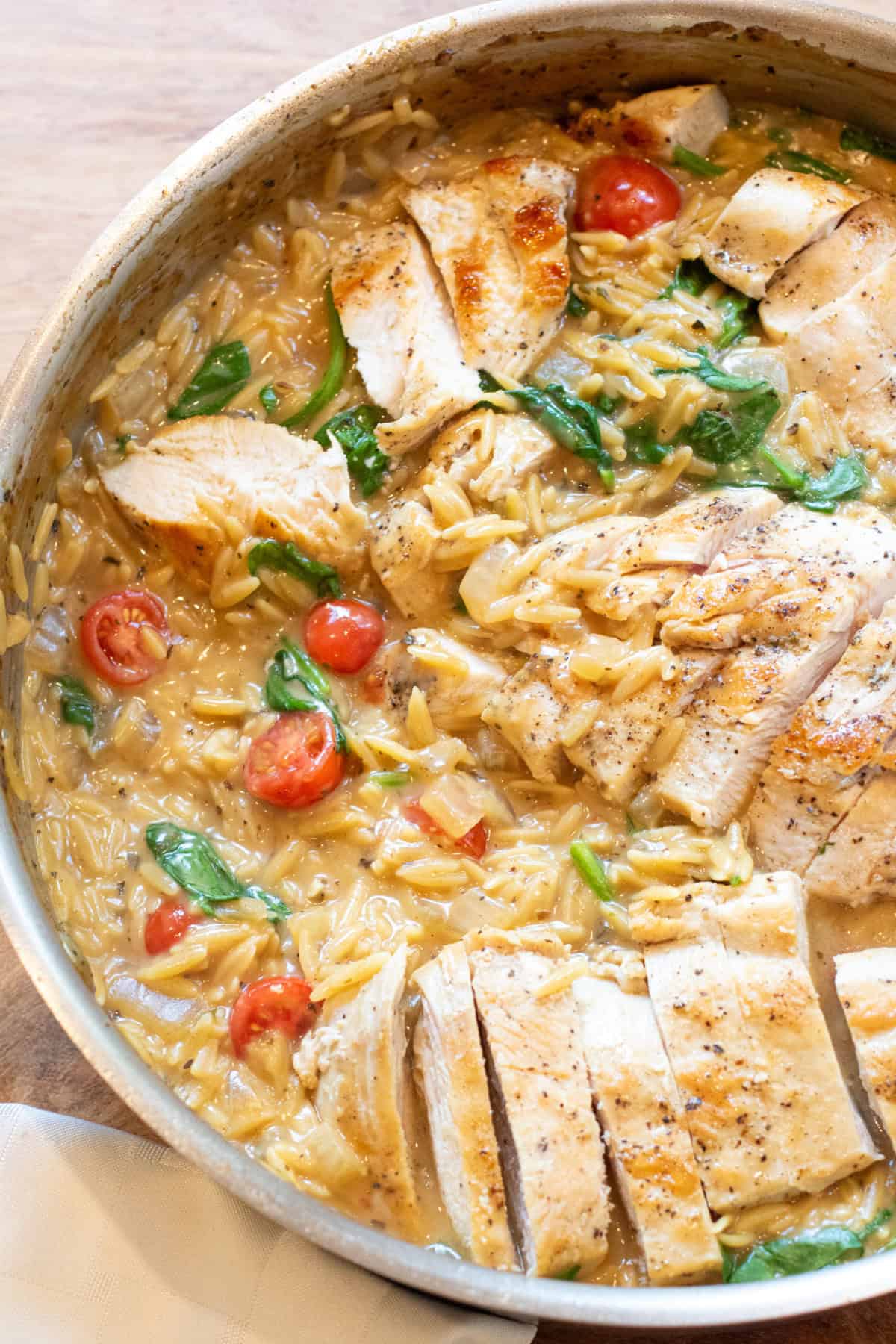 an overhead of a pan with cooked sliced chicken and creamy orzo, spinach, and tomatoes.