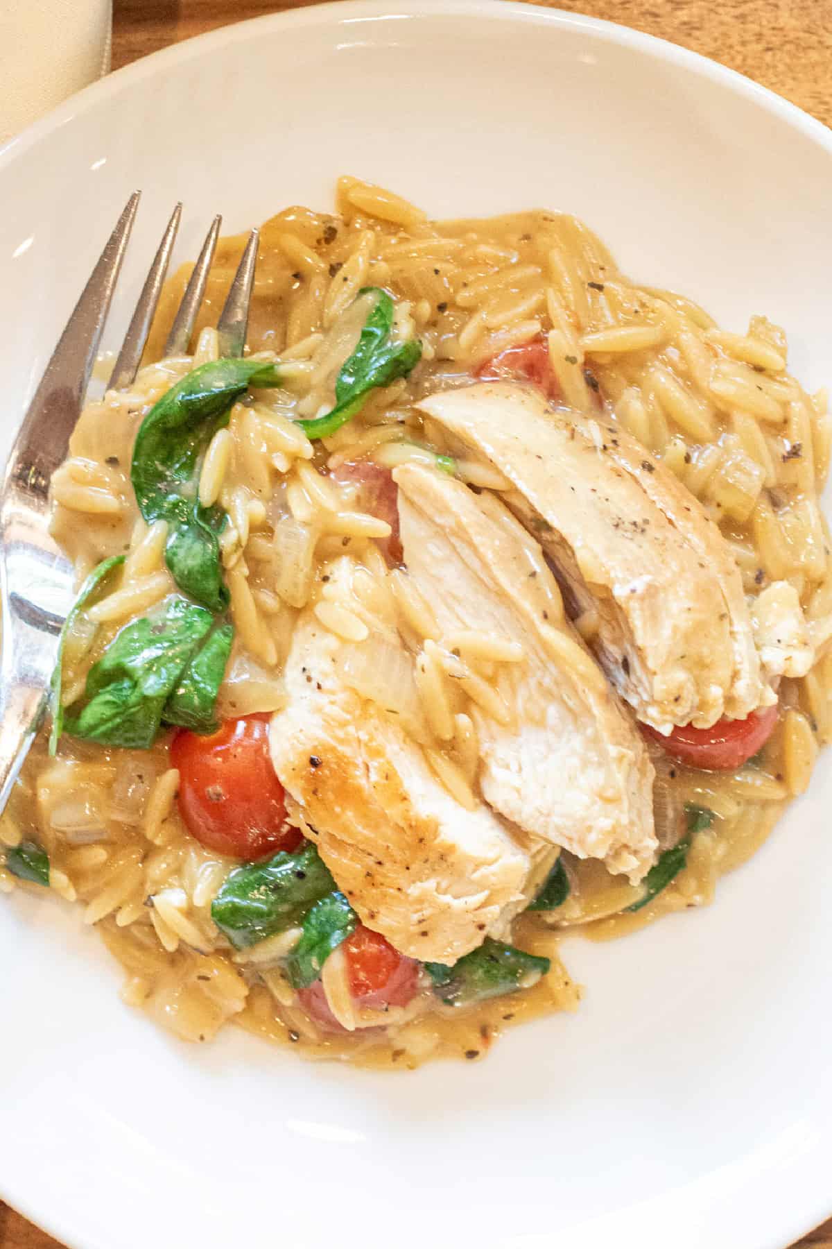 a plate of sliced chicken with creamy orzo spinach and tomatoes. 
