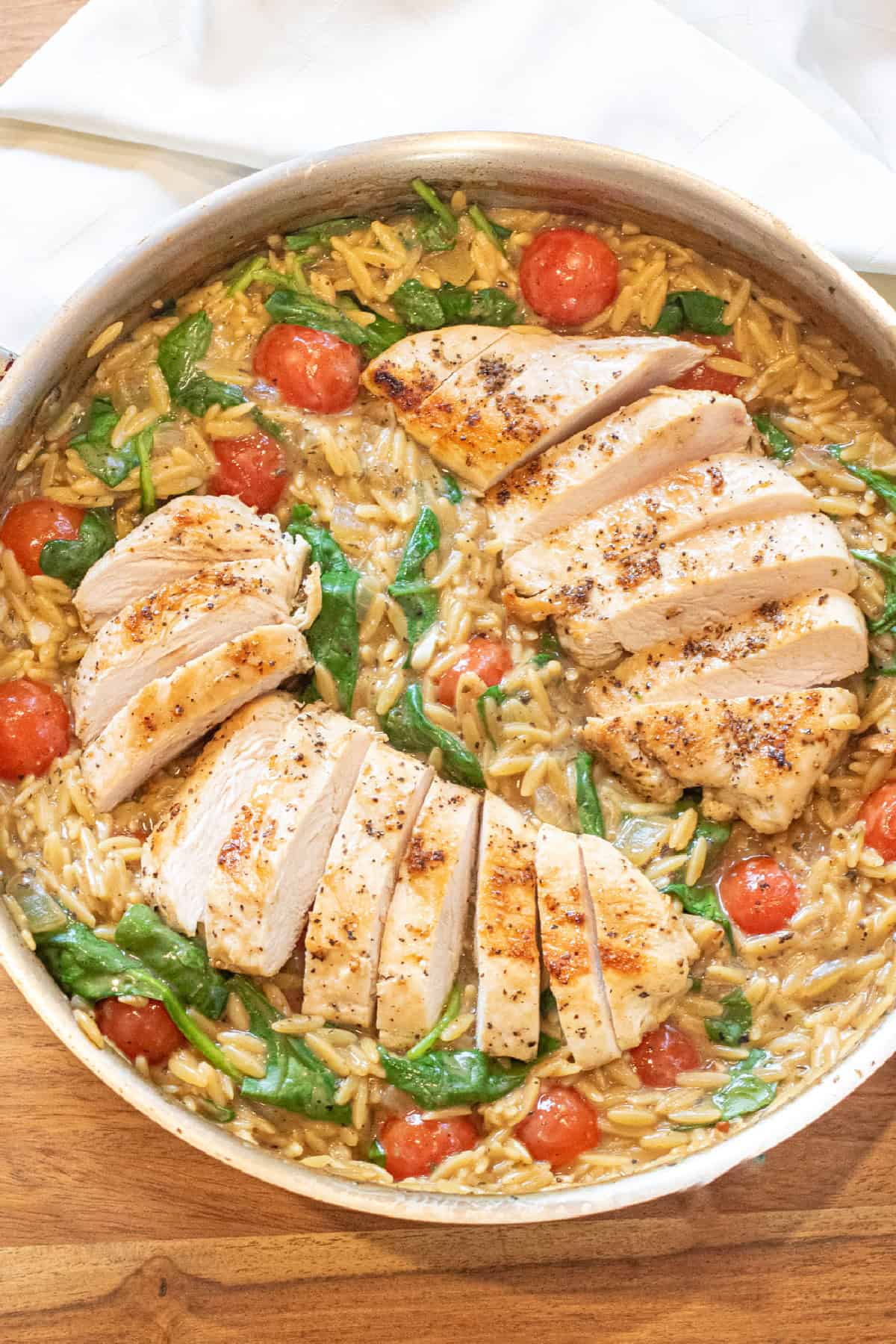 an overhead of a skillet with cooked sliced chicken and orzo and spinach and tomatoes.