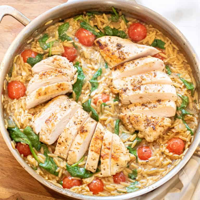 an overhead of a skillet with cooked sliced chicken and orzo and spinach and tomatoes.