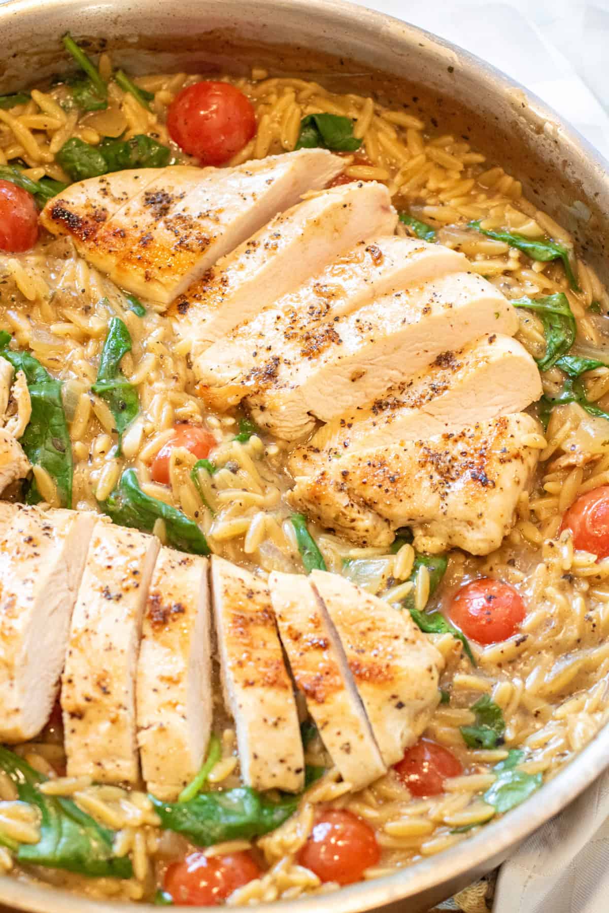 an overhead of a skillet with cooked sliced chicken and orzo and spinach and tomatoes.