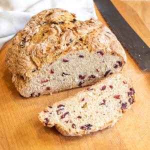 a loaf of bread with cranberries and a slice cut off with a bread knife.