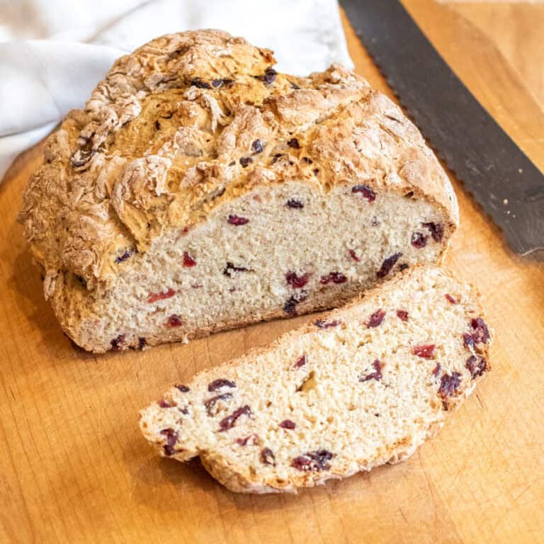 a loaf of bread with cranberries and a slice cut off with a bread knife.