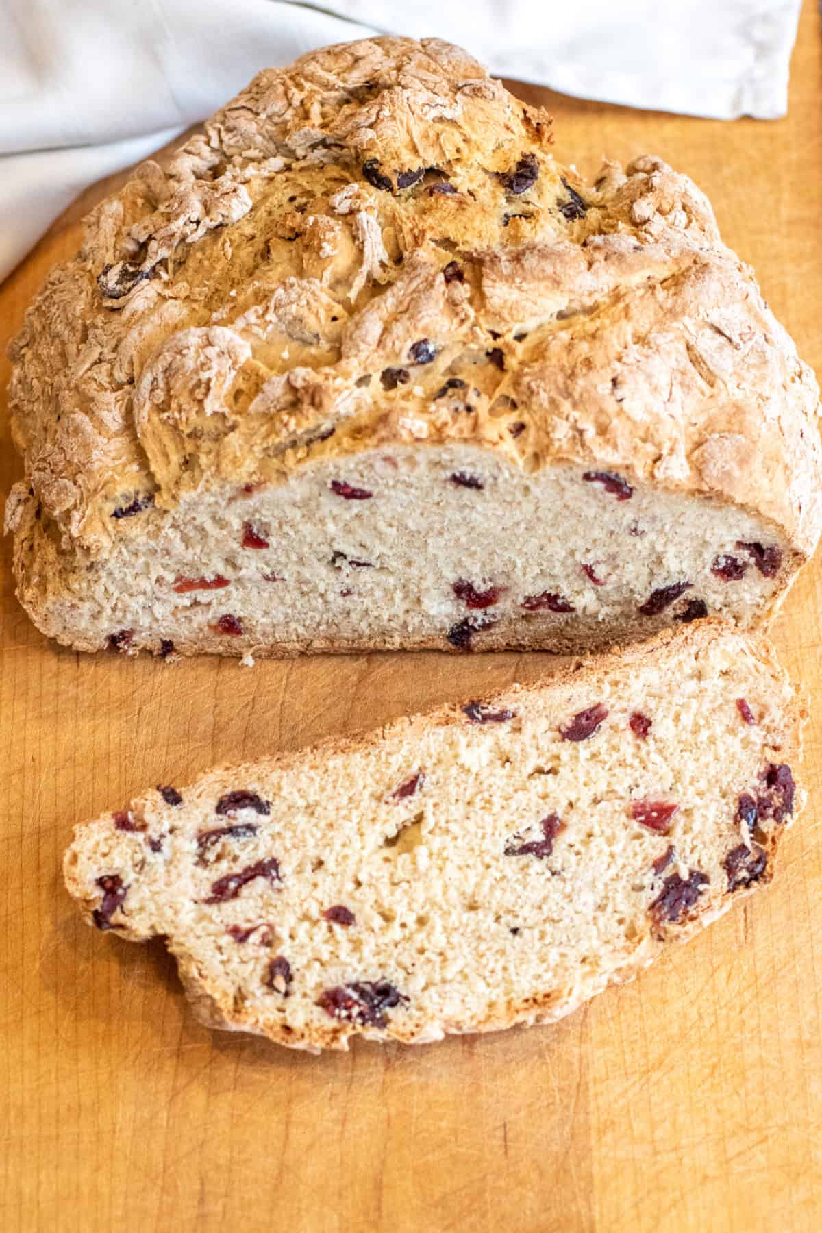 a loaf of bread with cranberries and a slice cut off with a bread knife.