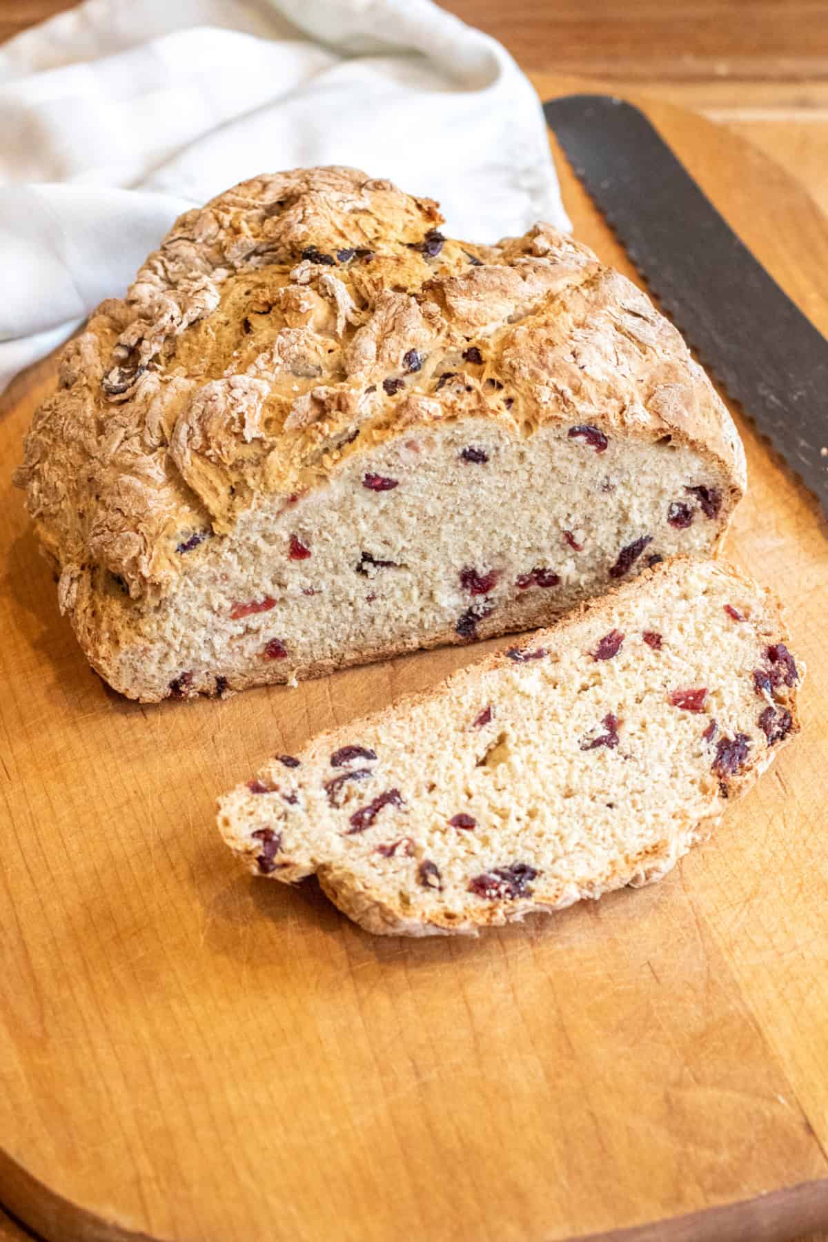 a loaf of bread with cranberries and a slice cut off with a bread knife.