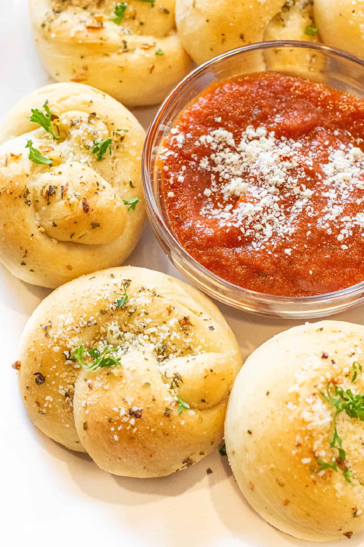 a plate of baked garlic knots with a bowl of marinara dipping sauce.