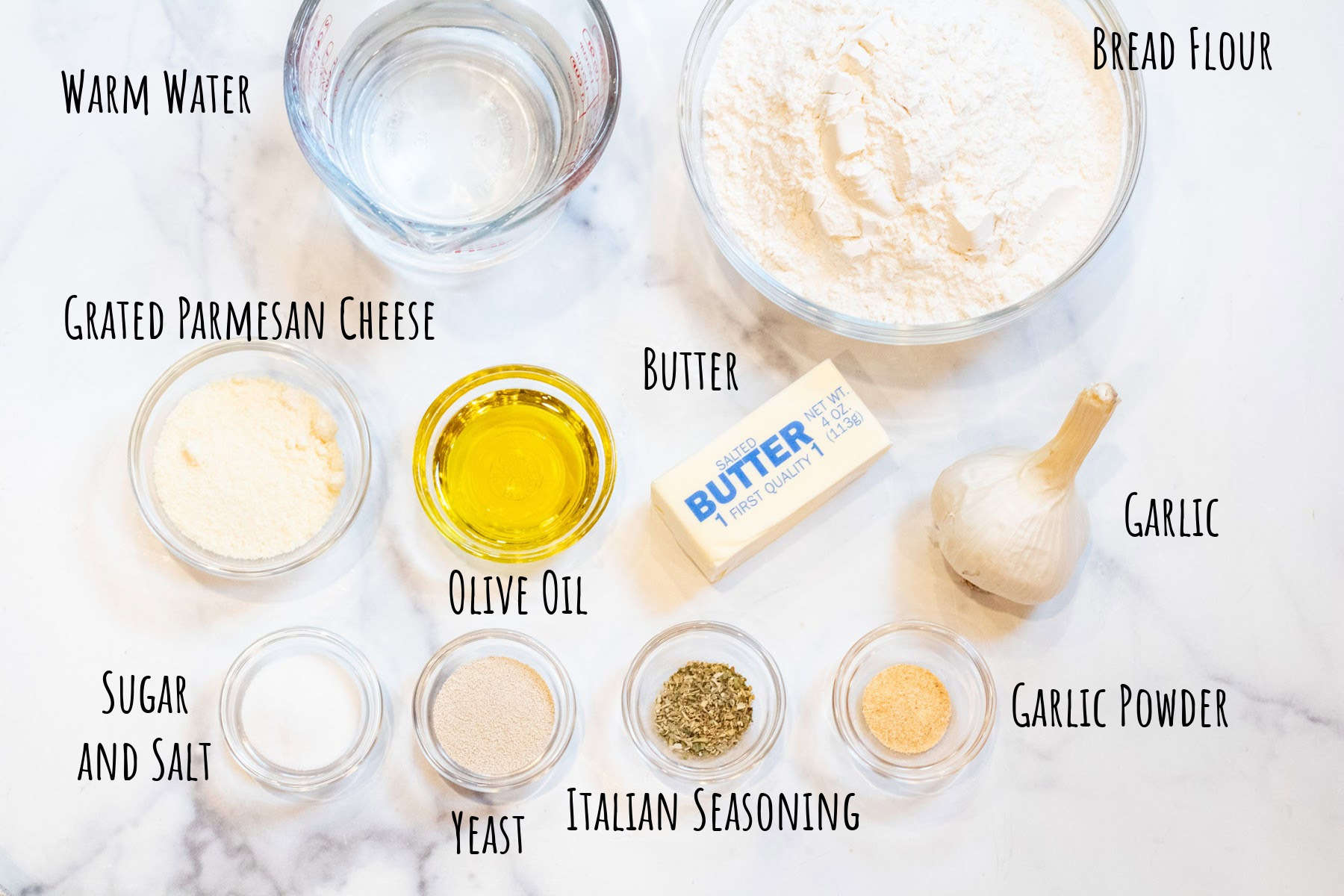 bowls of flour, salt, sugar, butter, garlic, oil, parmesan cheese, yeast, italian seasoning, and garlic powder labeled.