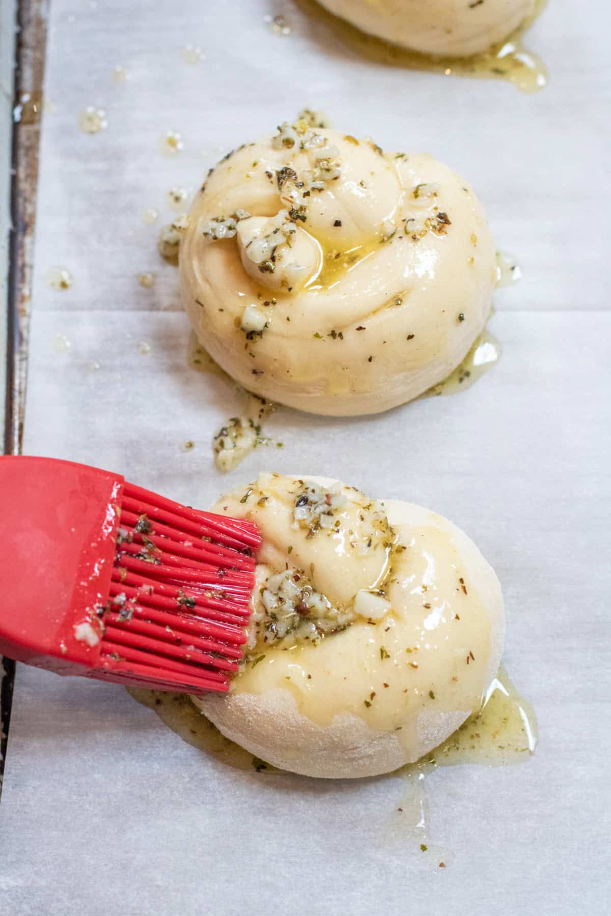 a brush brushing on butter and garlic and italian seasoning onto an unbaked garlic knot.