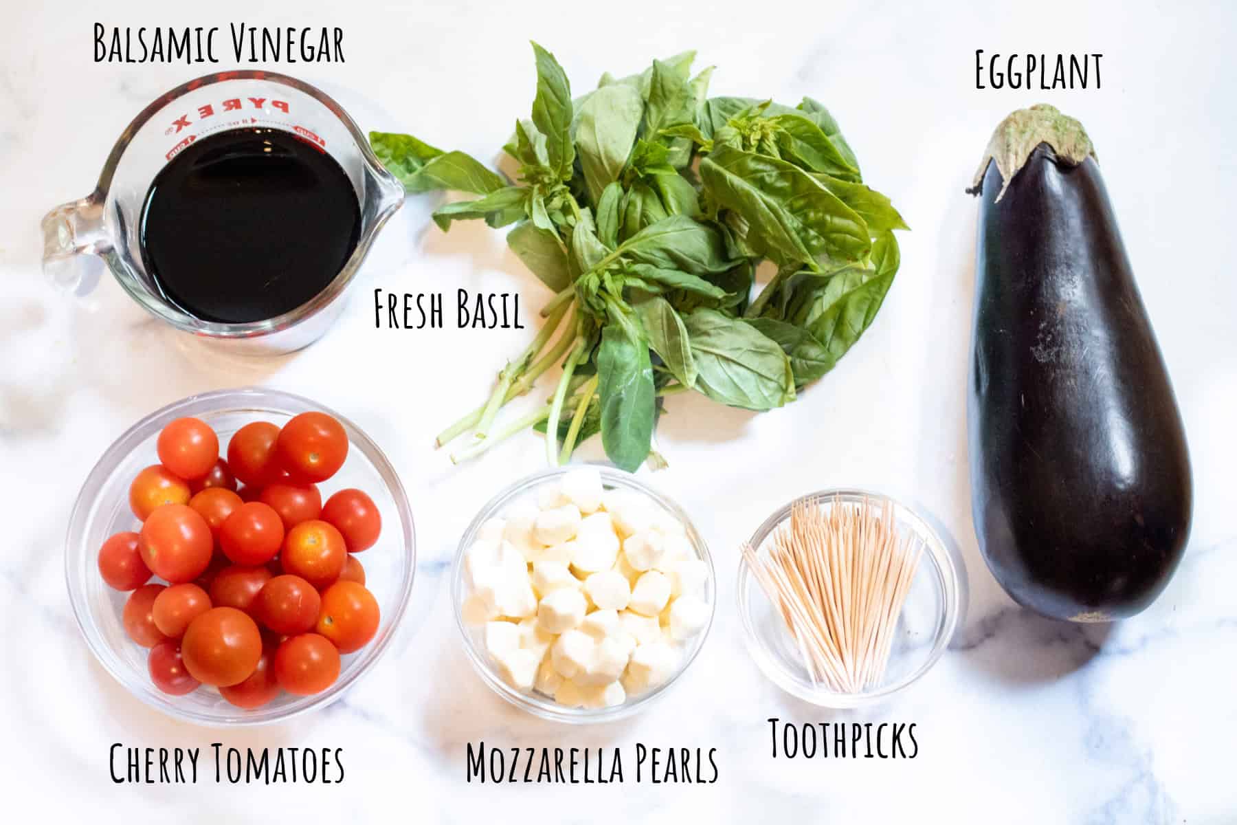 bowls of cherry tomatoes, mozzarella pearls, fresh basil, toothpicks, eggplant, and balsamic vinegar all labeled.