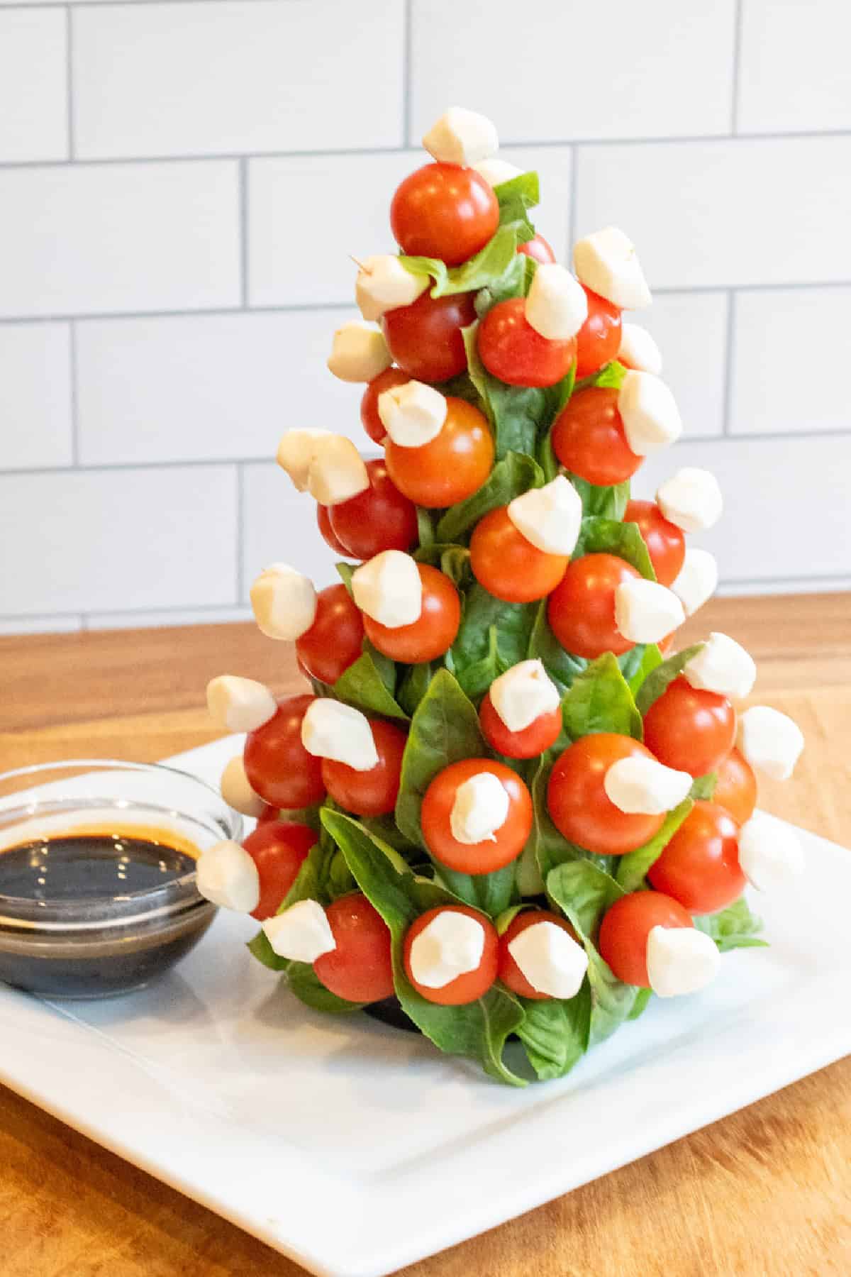 a christmas tree shaped caprese tree with a bowl of balsamic.