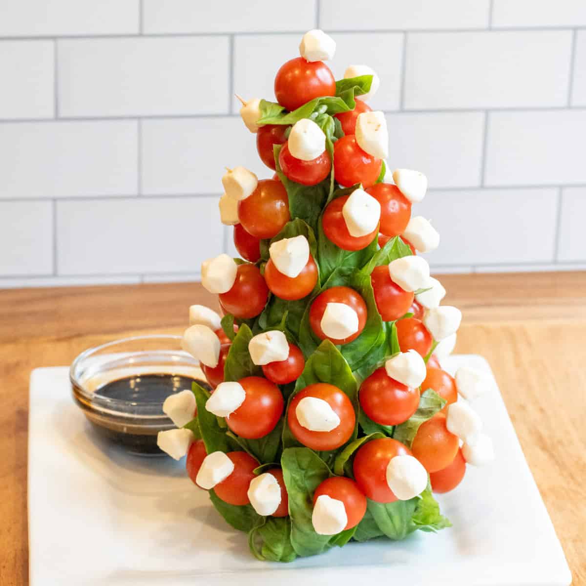 a christmas tree shaped caprese tree with a bowl of balsamic.