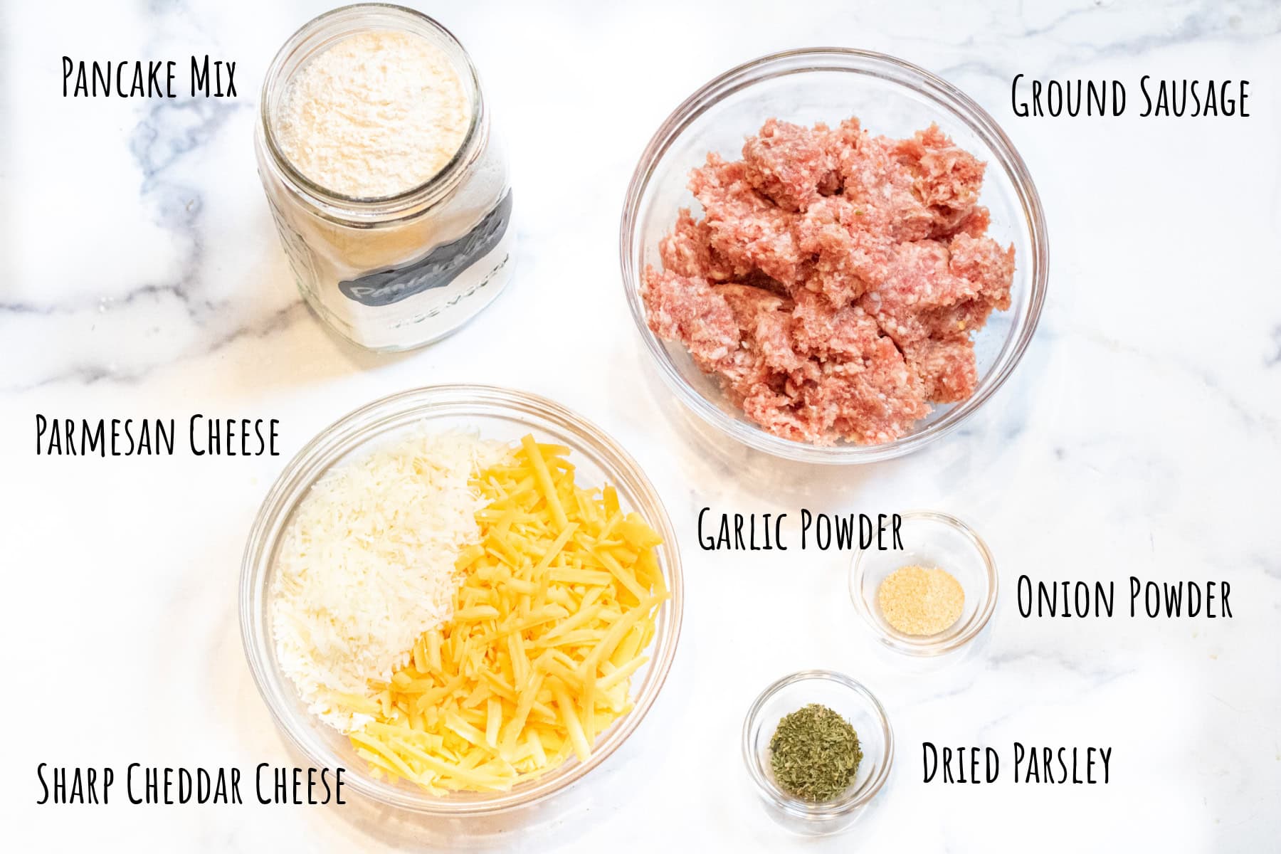 a container of pancake mix, and bowls of raw ground sausage, shredded cheeses and spices all labeled.