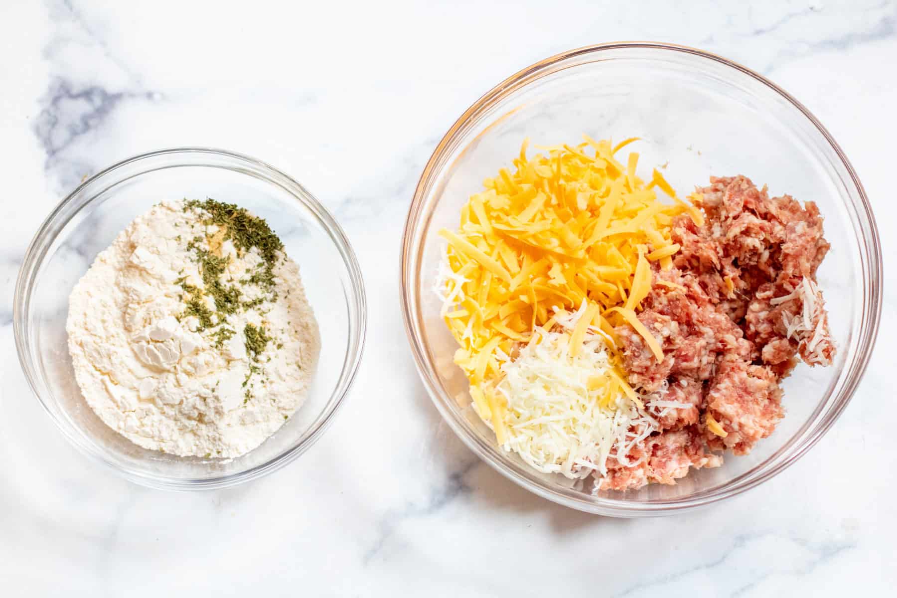 two bowls, one of pancake mix and spices and one of sausage and cheeses.