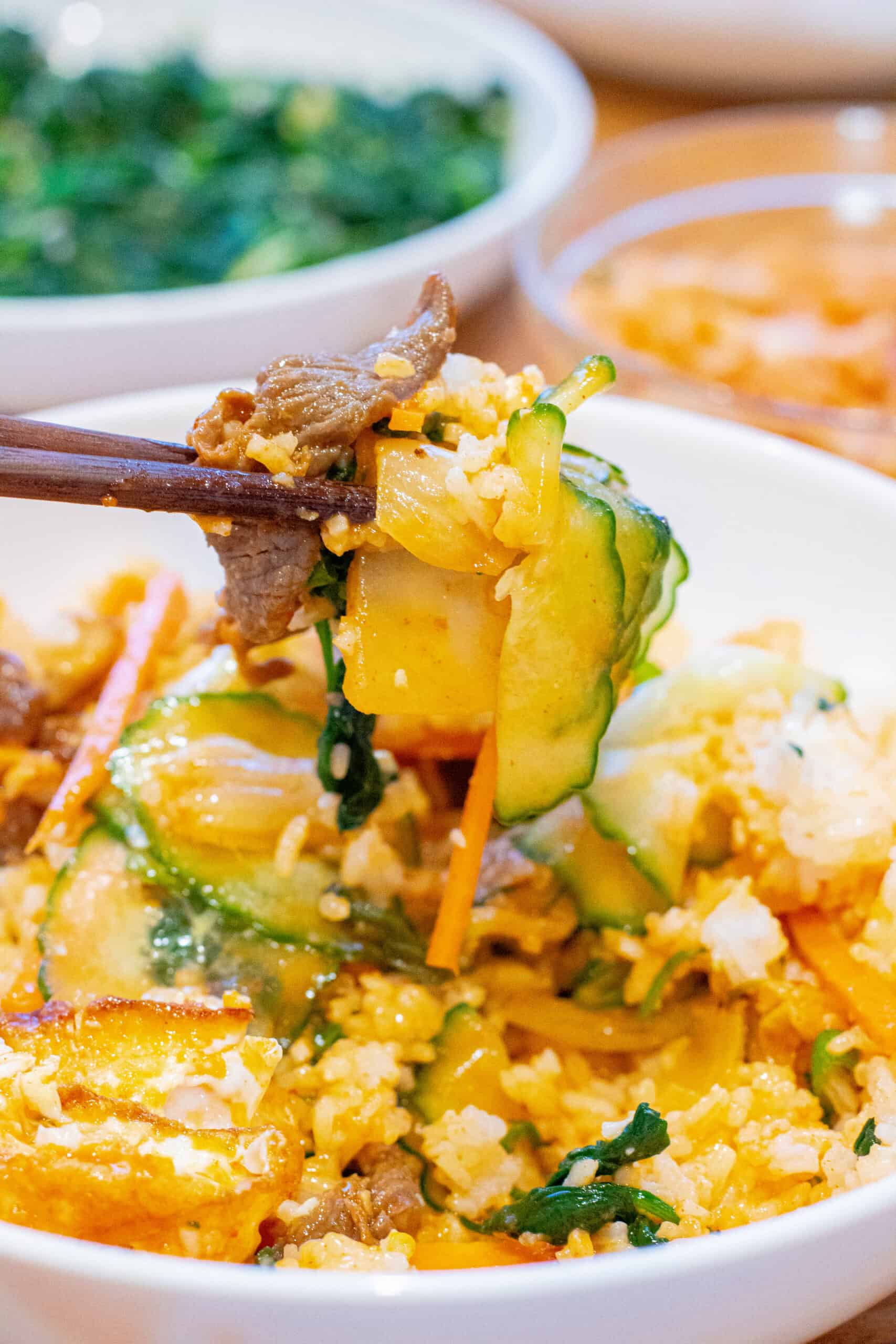 chopsticks holding up a bite of bibimbap over a bowl of it.