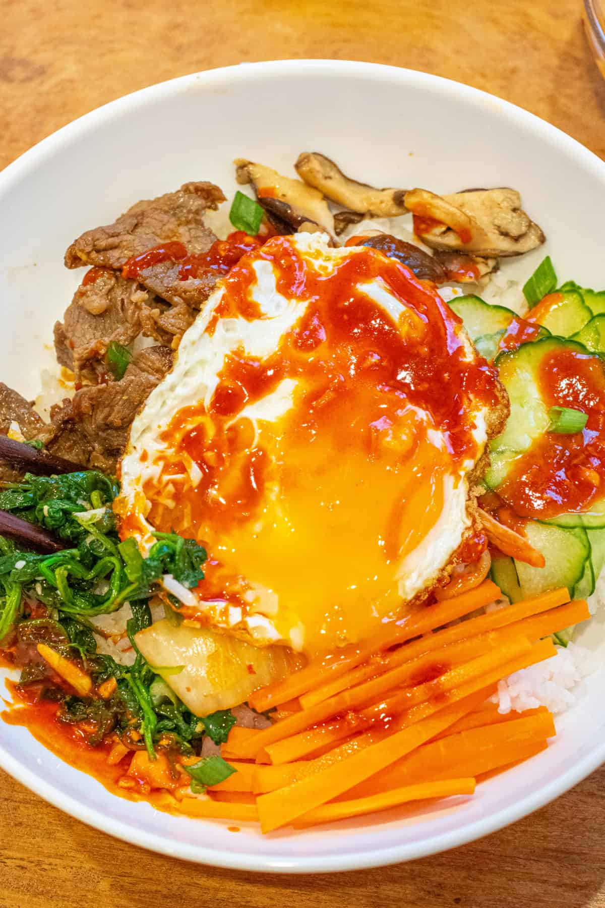 a bowl of bibimbap with the egg yolk broken.
