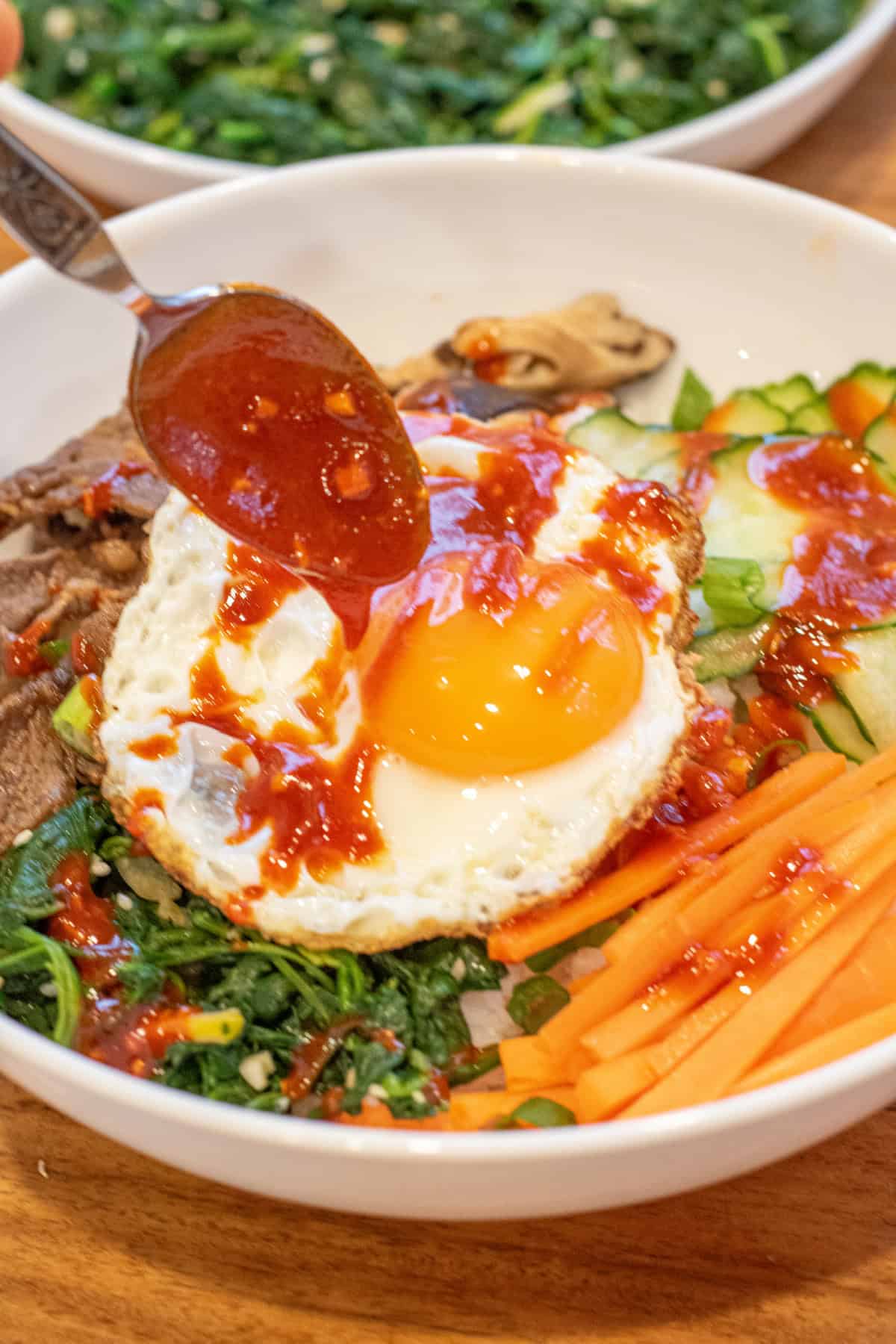 bibimbap sauce being spooned onto a fried egg in a bowl of bibimbap.
