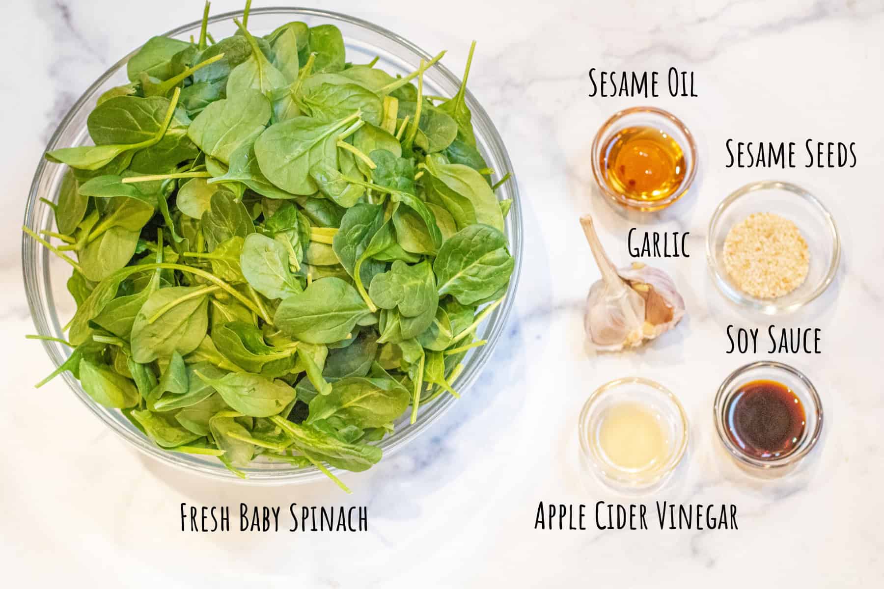a large bowl of fresh baby spinach and bowls of sesame oil, vinegar, garlic, soy sauce, sesame seeds.