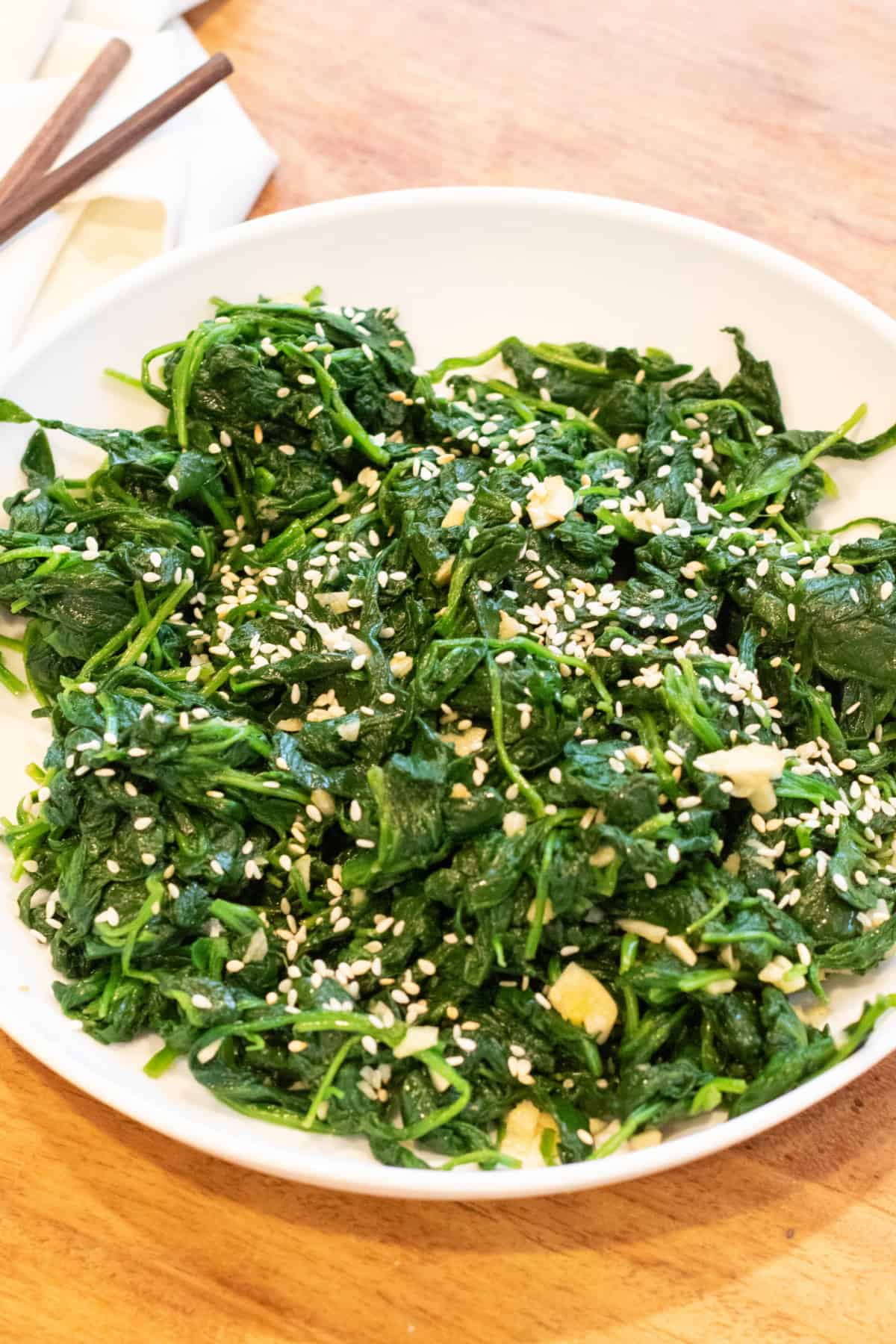 a bowl of blanched spinach with garlic and sesame seeds and chopsticks.