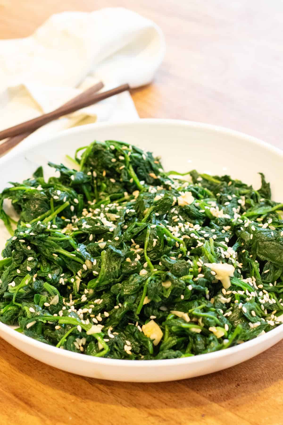 a bowl of blanched spinach with garlic and sesame seeds and chopsticks.