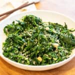 a bowl of blanched spinach with garlic and sesame seeds and chopsticks.
