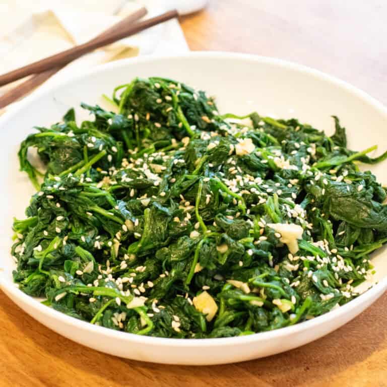 a bowl of blanched spinach with garlic and sesame seeds and chopsticks.